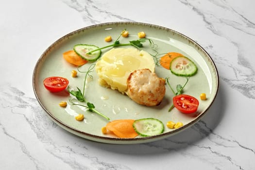 Delicious and healthy baked chicken patty with side dish of mashed potatoes garnished with slices of fresh carrot, cucumber, cherry tomatoes and green pea tendrils. Kids menu ideas concept