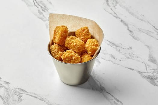 Golden crispy chicken nuggets in stainless steel bucket lined with parchment paper, presented on marble surface. Popular fast food dish
