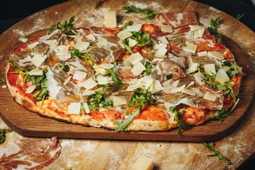 A freshly baked pizza with a golden crust and melted cheese is placed on a textured wooden cutting board.
