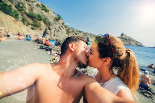 Loving couple kissing and taking selfies on the phone on the beach by the sea in the summer. Girlfriend and boyfriend on vacation