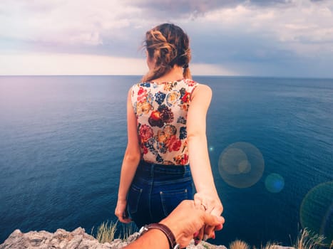girl holds her boyfriend's hand against the sea on a cliff on a summer day on a Hiking trip on vacation. Follow me