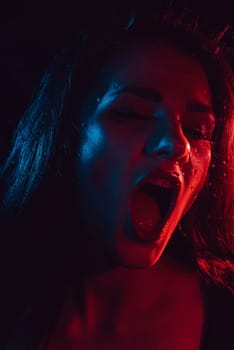 Sensual portrait of a screaming girl behind glass with raindrops and red blue light