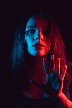 Sensual portrait of a beautiful attractive girl looking through the glass with raindrops with red blue lighting