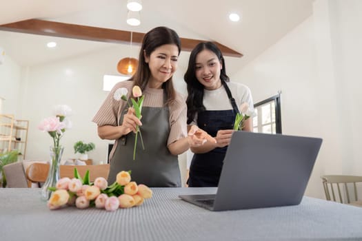 Happy mother and daughter arranging flower in vase at table in house do activities together on Mother's day.