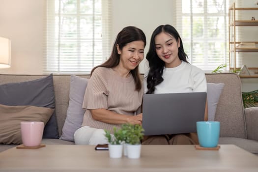 Happy mother and adult daughter use laptop having fun, sitting on couch at home, smiling woman embracing older mum, spending leisure time together. for Happy mother's day.
