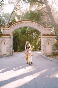 Laughing mother runs after a little girl along the park road at the gate. High quality photo