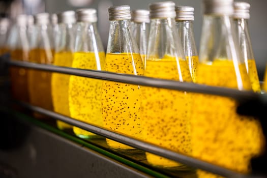 Basil or chia seed beverages with pomegranate undergo quality filling into transparent bottles on an automated conveyor belt in the beverage factory. Clean manufacturing ensures a healthy product.