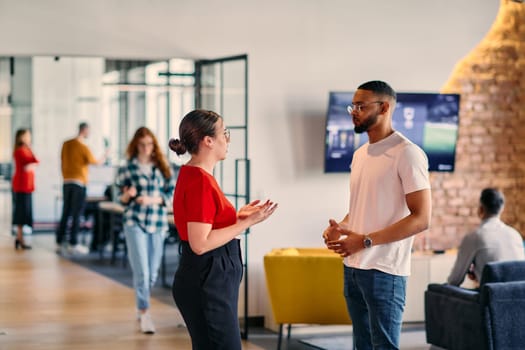 Young business colleagues, including an African American businessman, engage in a conversation about business issues in the hallway of a modern startup coworking center