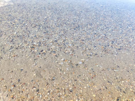 Pebbles in the water. Background, texture. Shallow Riverbed With Colorful Pebbles at Daytime. Clear water flowing over a multicolored pebble bed