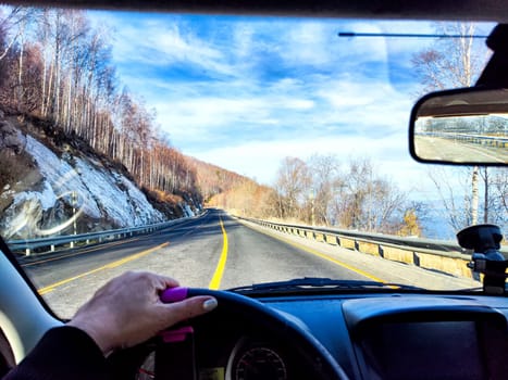 Car salon, windshield, hand of woman on steering wheel and landscape. View from seat of driver on nature landscape. Single trip of female traveler