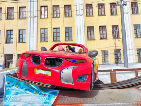 Kirov, Russia - March 17, 2024: People enjoy ride in whimsically designed flame-decorated carousel car. Amusement Ride Fun With Flaming Red Car