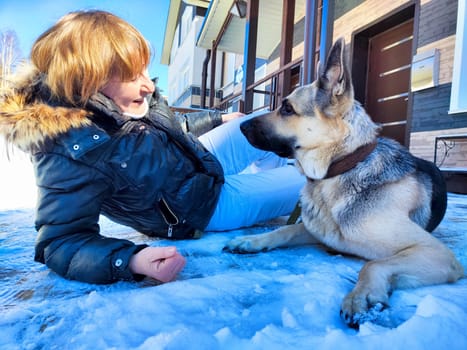 Adult girl or middle aged woman with shepherd dog near home in cold winter day with snow