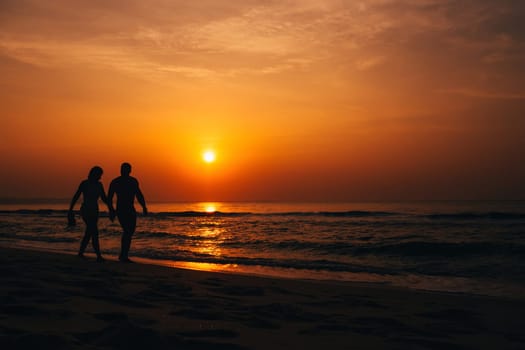 silhouettes of a couple walking along the beach by the sea at sunrise