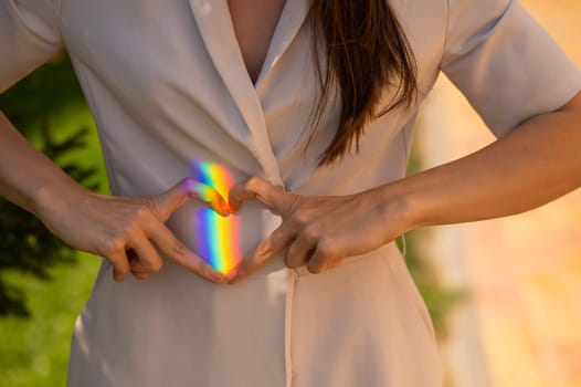 Faceless woman catching rainbow ray with her hands outdoors. Girl makes a heart with her hands