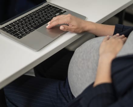 A pregnant woman works on a laptop in the office. Close-up of the tummy