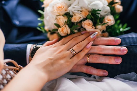 hands of the bride and groom with gold rings on the wedding day together on the background of the bouquet