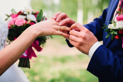 groom puts a wedding ring on the bride's finger at the wedding ceremony