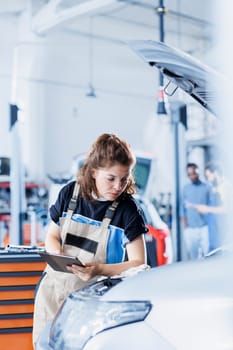 Meticulous repairman in car service uses tablet to calculate invoice for client after repairing fuel tank. Focused garage specialist calculating final costs after servicing customer vehicle