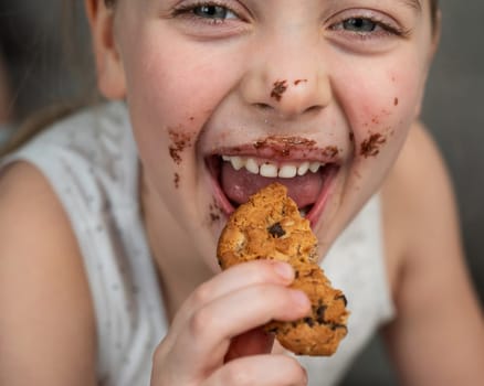 A cute little girl smeared in chocolate eats cookies while lying on the sofa