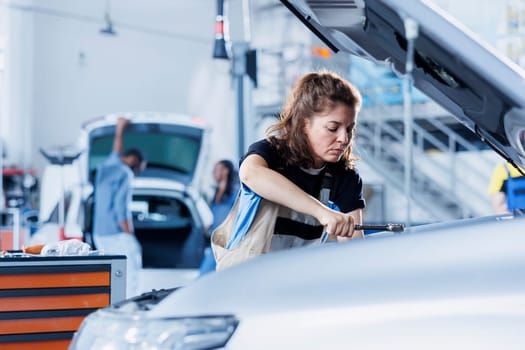 Woman in car service using professional mechanical tool to repair broken exhaust system. Skillful mechanic in garage fixing client automobile, ensuring optimal automotive performance