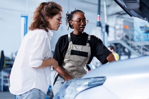Mechanic at auto repair shop conducts annual vehicle checkup, informing customer about needed compressor belt replacement. Adept garage worker talks with customer after finishing car inspection