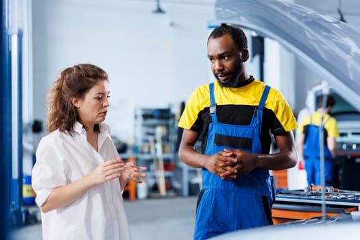 Friendly engineer helping client with car checkup in auto repair shop. Garage worker looking over automobile parts with woman, mending her defective vehicle fuel tank during inspection