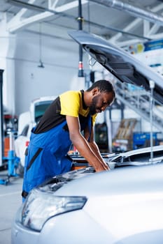 Engineer expertly examines car motor using advanced mechanical tools, ensuring optimal automotive performance and safety. African american garage employee conducts annual vehicle checkup
