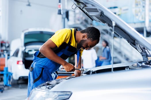 Engineer expertly examines car brakes using advanced mechanical tools, ensuring optimal automotive performance and safety. BIPOC licensed garage employee conducts annual vehicle checkup