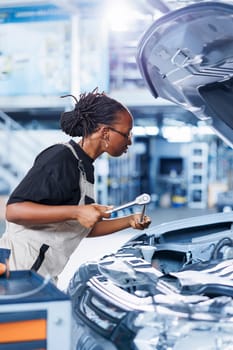 Repair shop technician expertly examines car motor using advanced mechanical tools, ensuring proper automotive performance. Focused professional in garage workplace conducts routine vehicle checkup