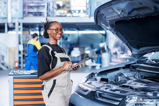 Portrait of proud BIPOC serviceman holding tablet in auto repair shop tasked with changing cars oil. Skilled woman in garage ready to start doing checkups on vehicles in garage workspace