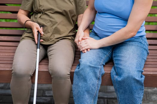 An elderly blind woman and her pregnant daughter are sitting on a bench in the park. Close up legs