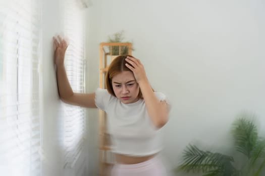 Dizzy asian young woman, woman headache or migraine pain. suffering from vertigo, difficulty standing up leaning on wall at home.