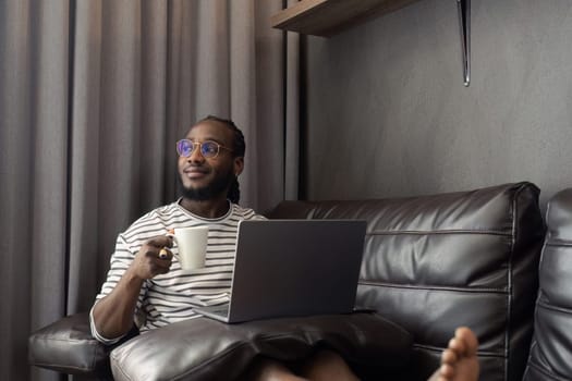 young attractive african working at home and use laptop checking schedule working and relax on sofa in living room with morning light peaceful moment.