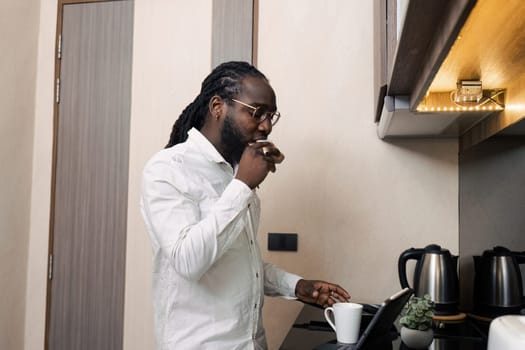 African businessman eat sandwich in the morning and use a tablet to work on company documents. While working online from home.