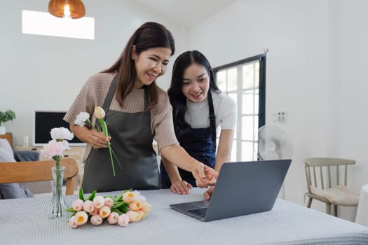 mother and daughter arrange flowers together as a hobby. mother and daughter spend free time doing flower arranging activities together and looking at laptop.