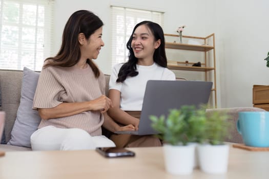 Mother and adult daughter sitting on the sofa together, mother and daughter using laptop to surf website together.