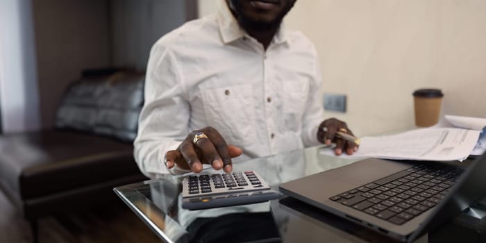 Business African man using a calculator to calculate numbers on a company's financial documents at home. work from home concept.