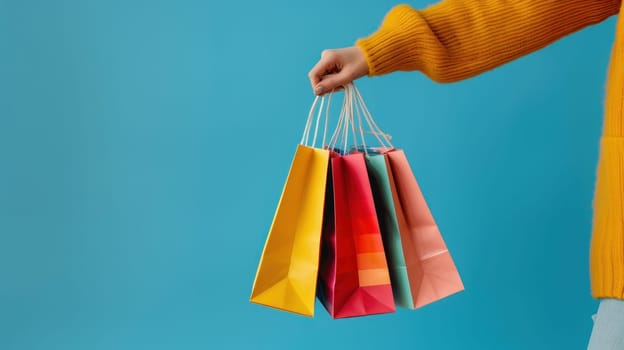 Close up of a woman's hand holding colorful shopping bags isolated on a blue background.