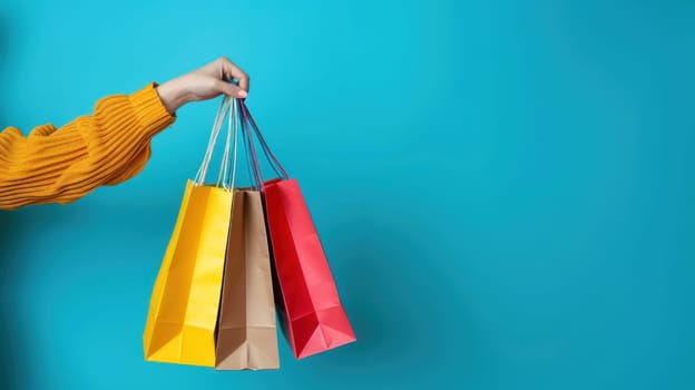 Close up of a woman's hand holding colorful shopping bags isolated on a blue background.