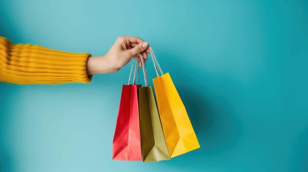 Close up of a woman's hand holding colorful shopping bags isolated on a blue background.