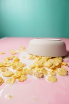 Bowl with corn flakes and milk spilling on table .