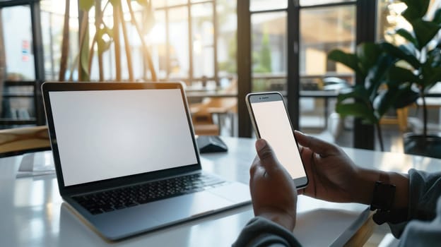 Mockup empty, a person is working on a laptop with a white screen, another person is holding a phone with a white screen, modern office in the background.