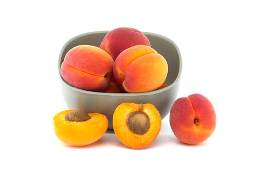 Bowl filled with fresh whole apricots and one cut in half to reveal its interior, isolated on a white background