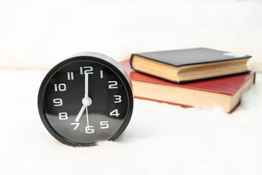 Close up Black alarm clock and book stacked on table