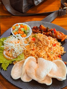 Fired rice or nasi goreng Indonesian chicken fried rice served with pickled cucumber and onion and chili with prawn crackers with satay as condiment on grey plate