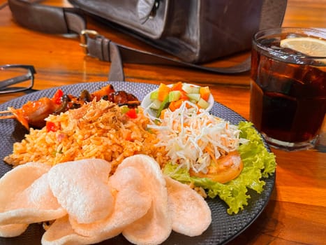 Fired rice or nasi goreng Indonesian chicken fried rice served with pickled cucumber and onion and chili with prawn crackers with satay as condiment on grey plate