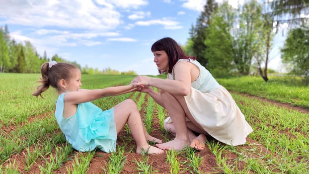 Happy mother and daughter enjoying rest, playing and fun on nature in green field. Woman and girl resting outdoors in summer or spring day