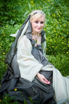 Adult mature woman 40-60 in a green long fairy dress in forest. Photo shoot in style of dryad and queen of nature. Fairy in beautiful green summer forest. Concept of caring for nature