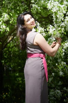 Joyous brunette woman near Blossoms of apple tree in a Spring Garden outdoors. The Concept of face and body care. The scent of perfume and tenderness