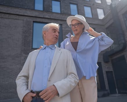 A woman in a hat and glasses hugs an elderly man in a white jacket from behind. Romantic relationships of mature people